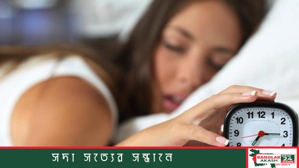 একটি স্মার্টফোনের স্ক্রিনে বাজতে থাকা সকালের অ্যালার্মের ঘড়ি ও বিছানায় ঘুমন্ত ব্যক্তি।